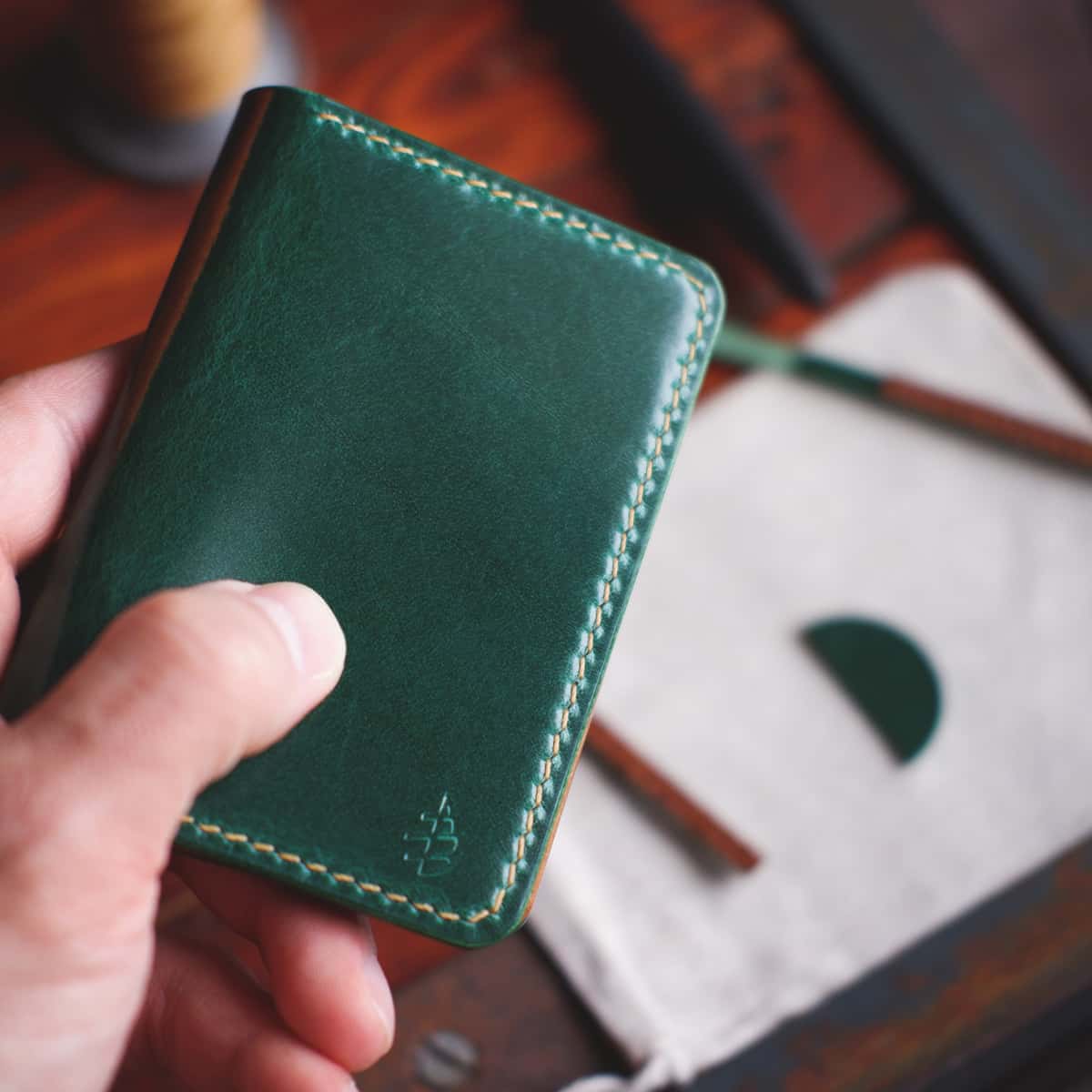 The Monterey 4-Slot Bifold wallet in Emerald Green Gaucho Oil leather held in hand